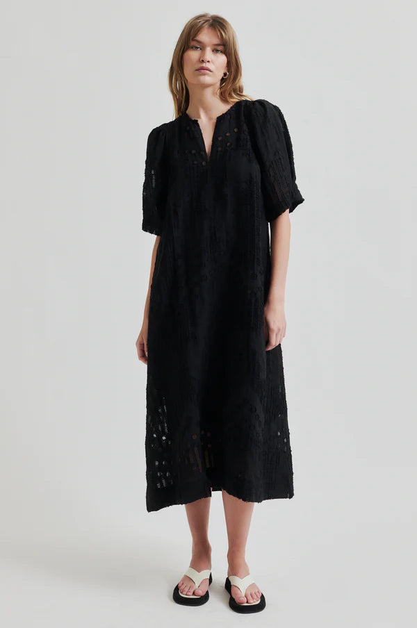 Intricate woven black midi dress with v neck and puff sleeves on model paired with cream sandals. 