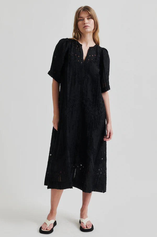Intricate woven black midi dress with v neck and puff sleeves on model paired with cream sandals. 