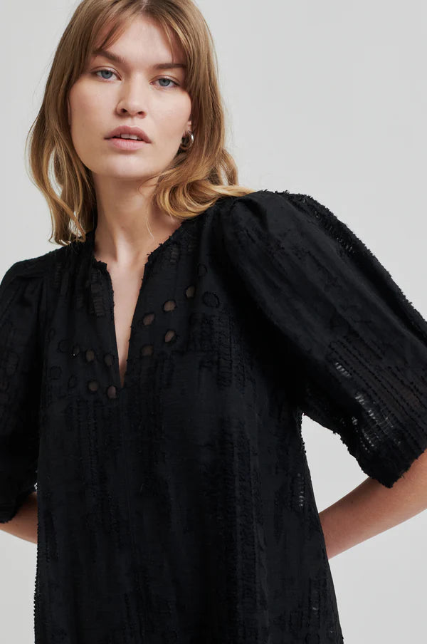 Intricate woven black midi dress with v neck and puff sleeves close up on model. 
