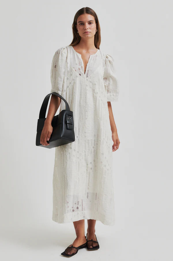 Woman wearing a long off white dress with embroidery detail with short sleeves