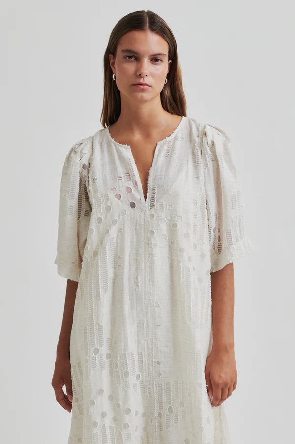 Woman wearing a long off white dress with embroidery detail with short sleeves