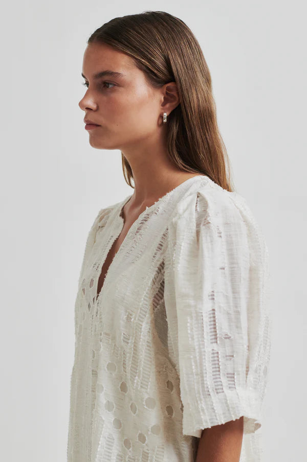 Woman wearing a long off white dress with embroidery detail with short sleeves