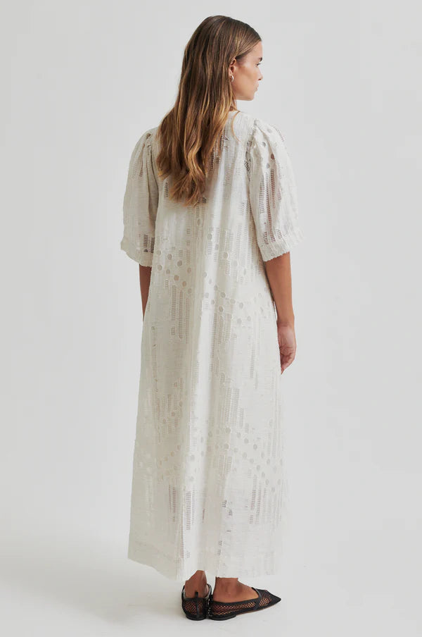 Woman wearing a long off white dress with embroidery detail with short sleeves
