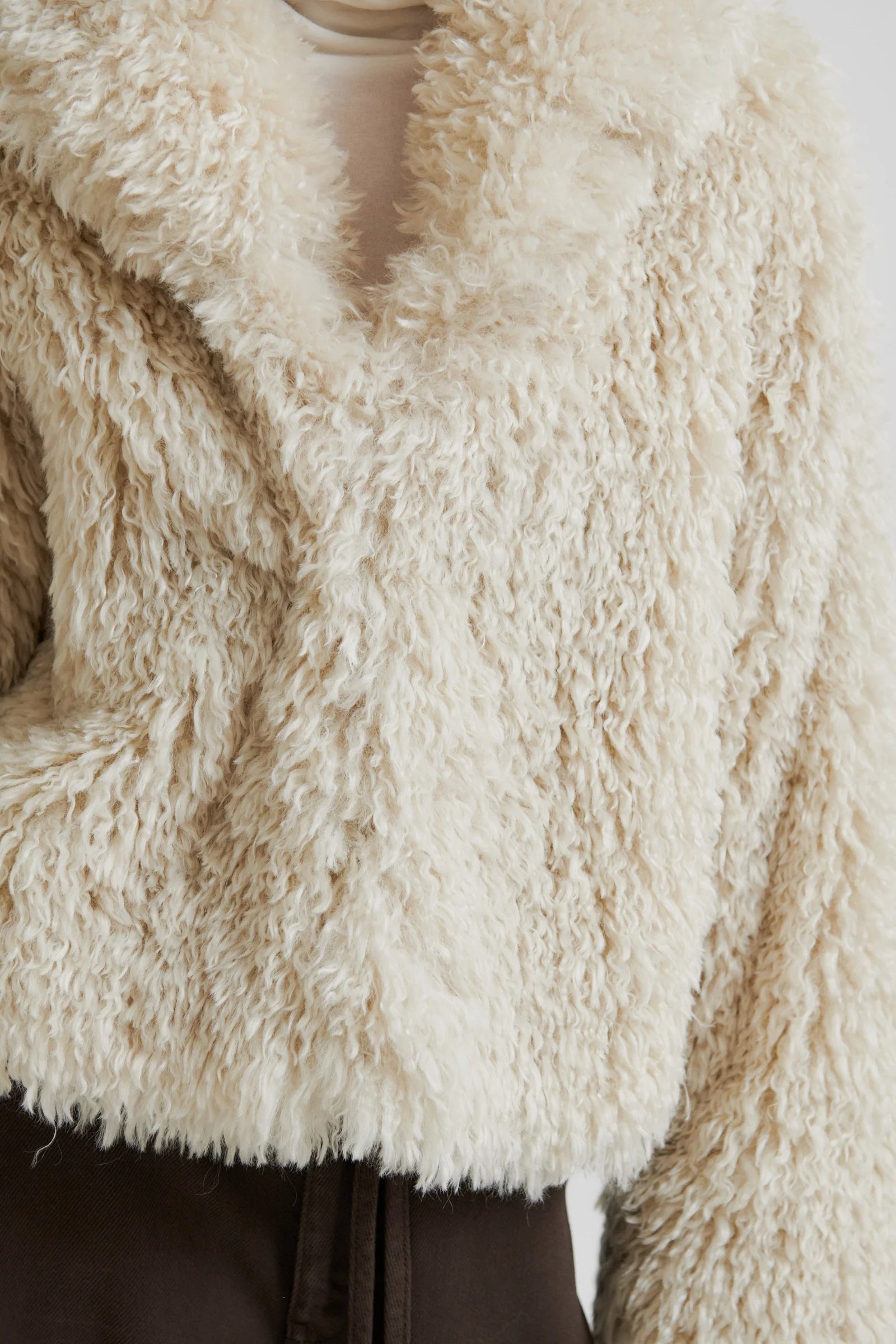Close-up of a beige fluffy jacket with chocolate brown pants. 
