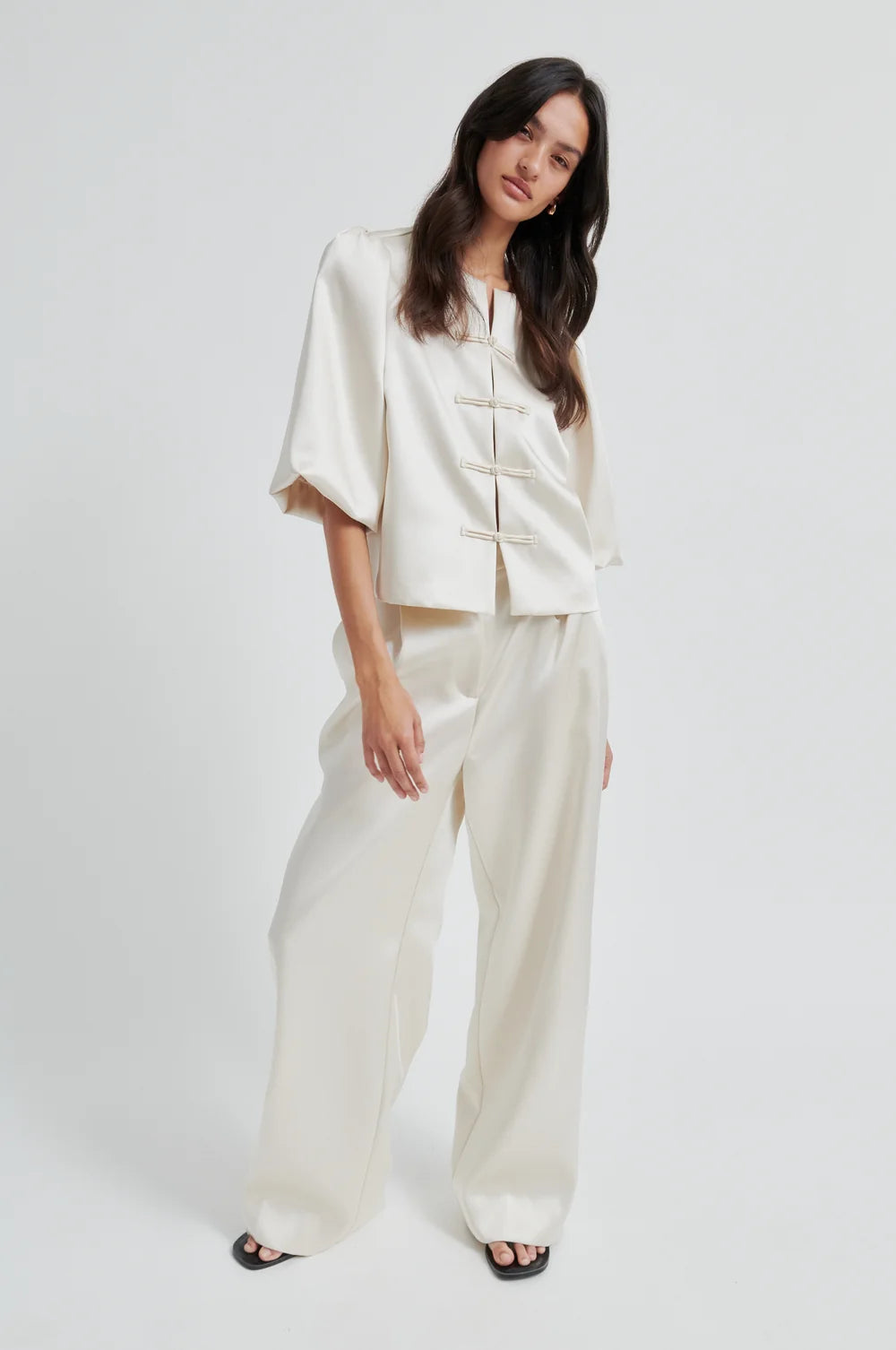 Woman wearing a beige short sleeve blouse with ballon sleeves and matching pants on a plain background