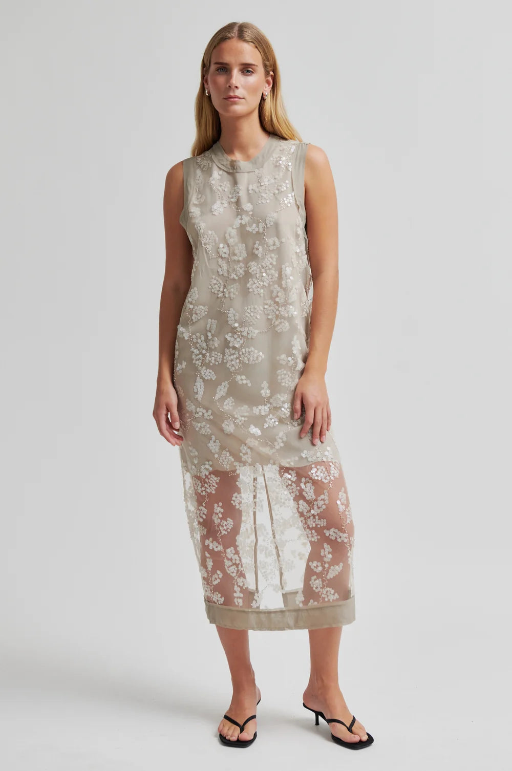 Woman wearing a sleeveless floral dress  with lace detailing on a plain background