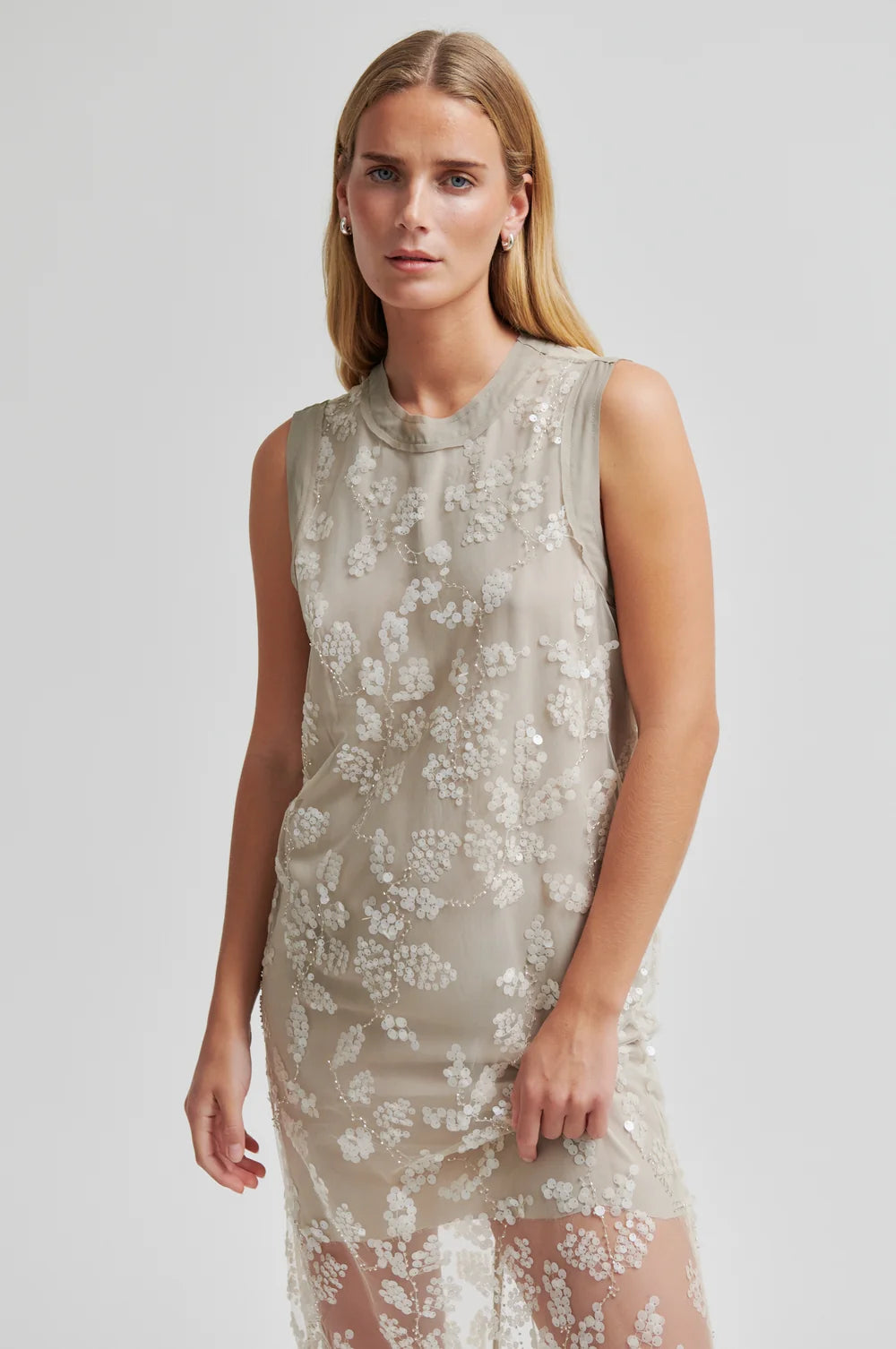 Woman wearing a beige loral lace dress against a plain background