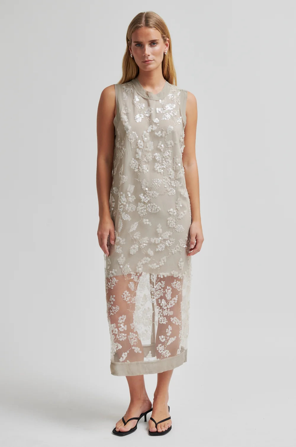 Woman wearing a sleeveless lace dress on a plain background
