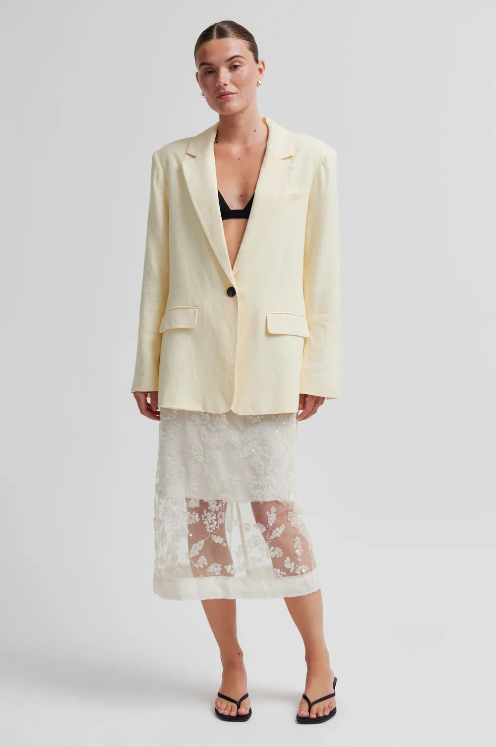 Woman wearing a light yellow blazer over a lace dress on a white background