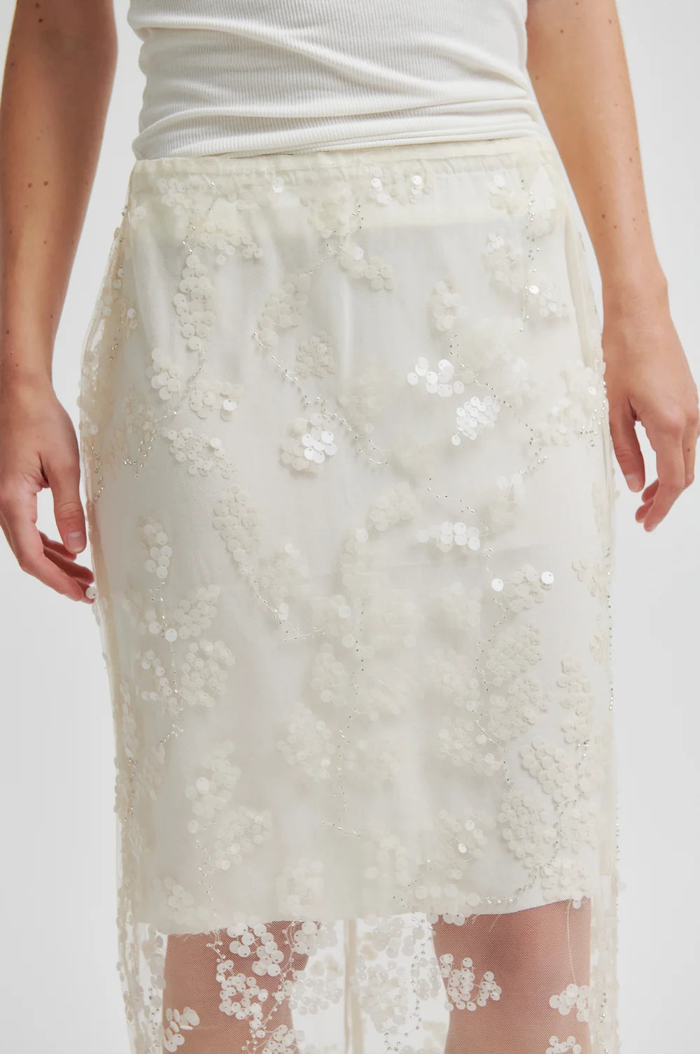 White lace skirt worn by a person on a plain background