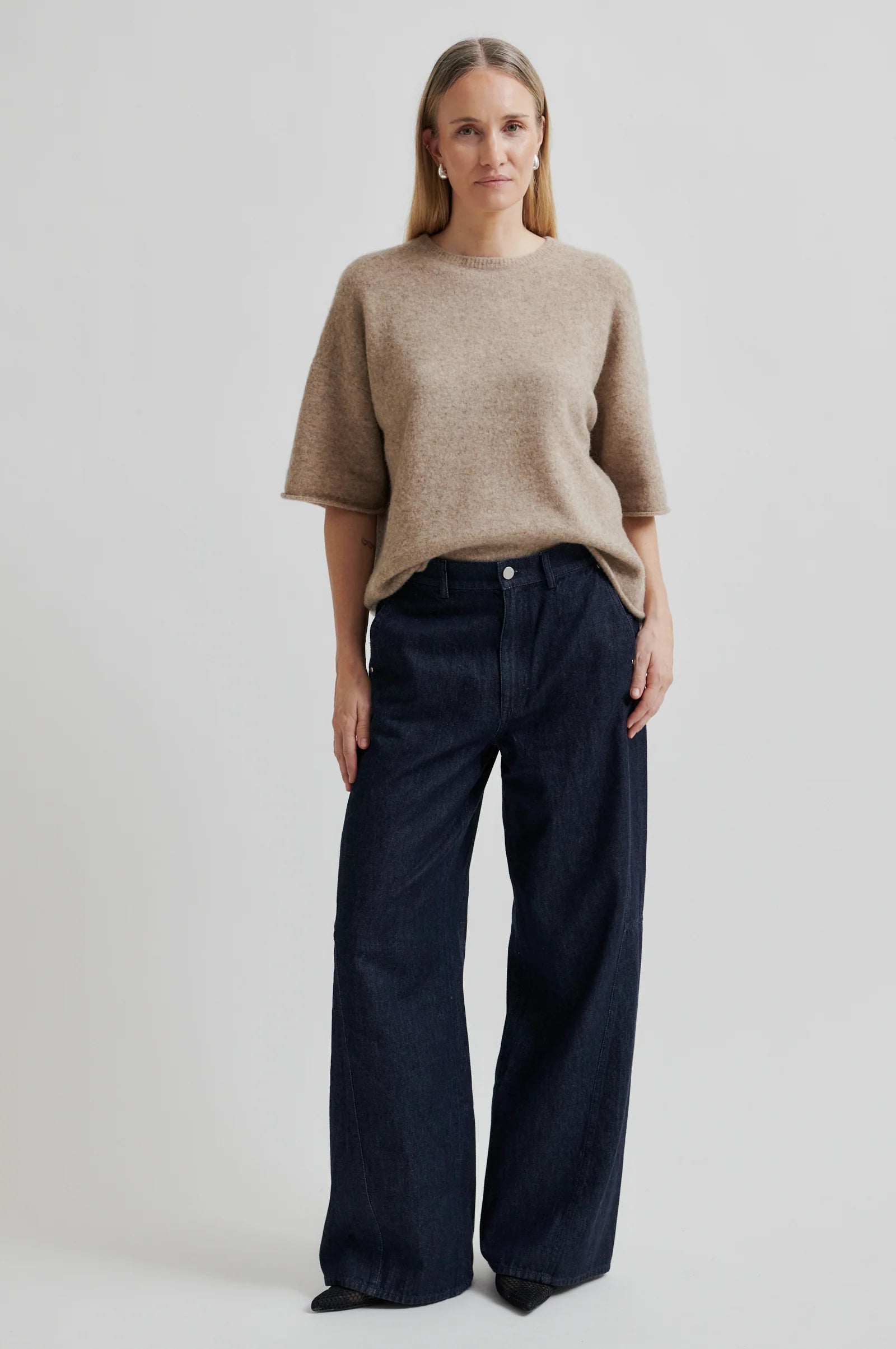 Woman wearing a beige short sleeve sweater and denim wide leg pants on a white background