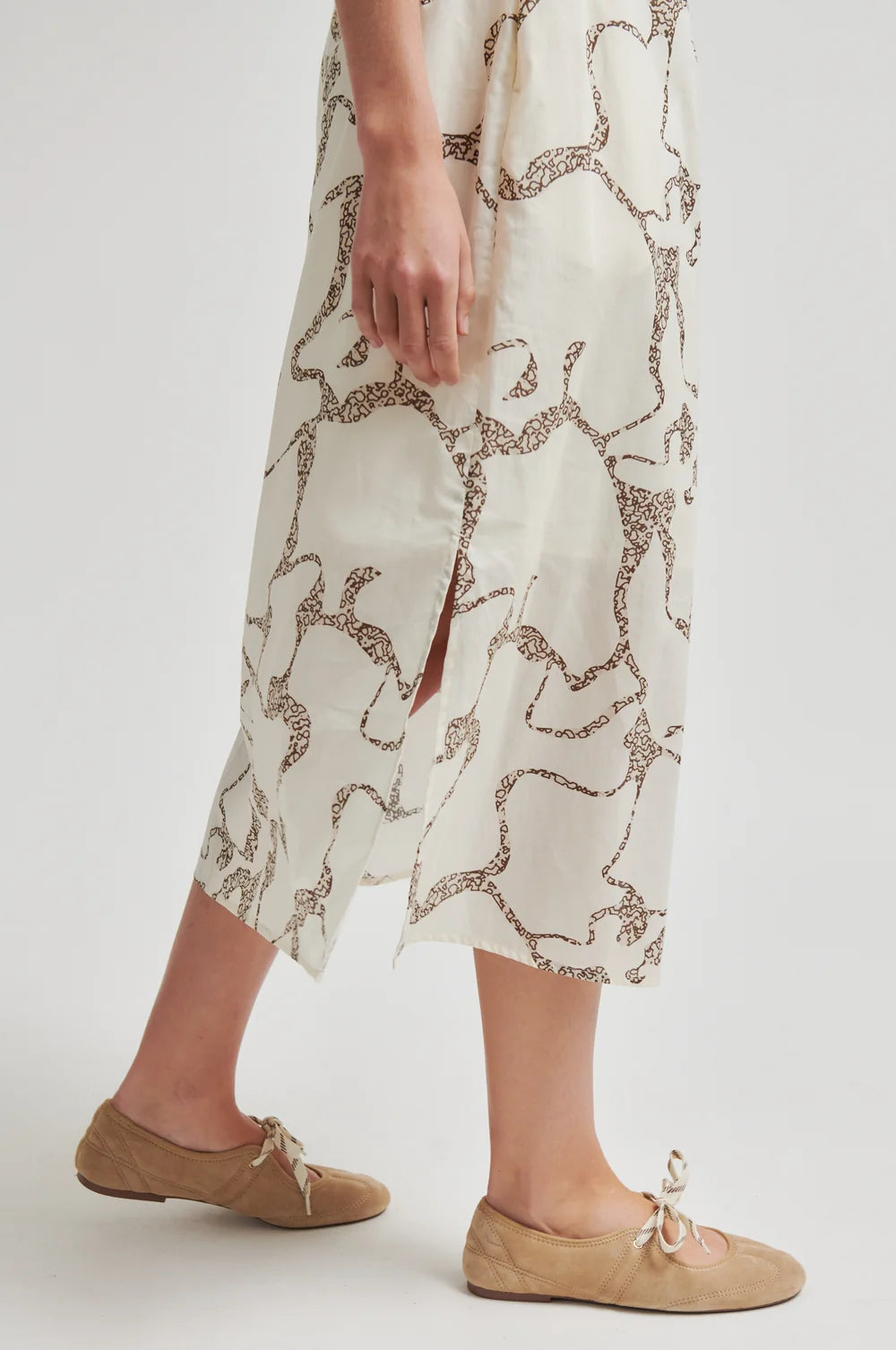 Person wearing a patterned skirt and beige shoes on a white background