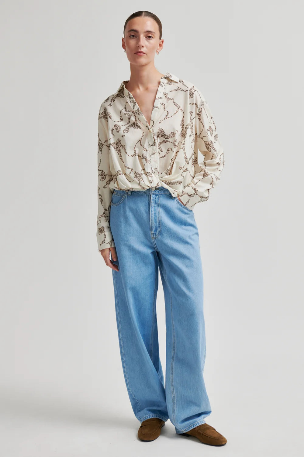 Person wearing a patterned blouse and blue jeans on a white background