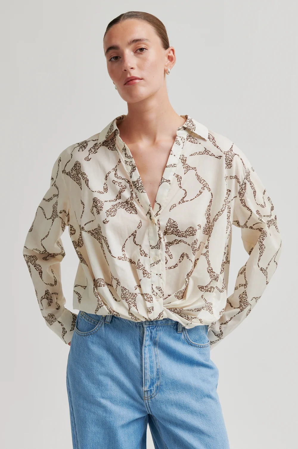 Person wearing a patterned blouse and blue jeans on a plain background