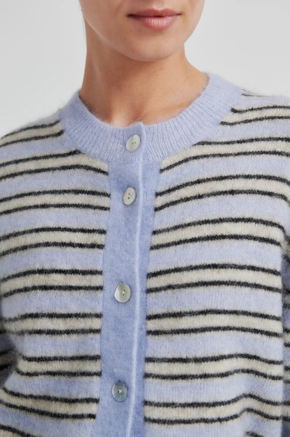 Woman wearing a blue cream and brown striped short sleeve cardigan and wide-leg pants with a black handbag on a light background