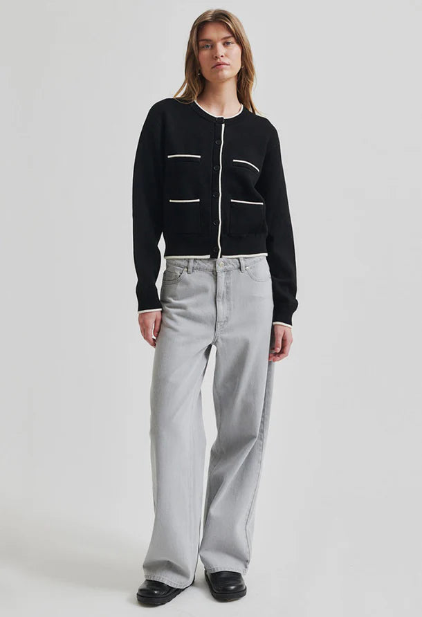 Black cardigan with white accents round collar and button through front paired with wide leg grey denim jeans and black shoes. 
