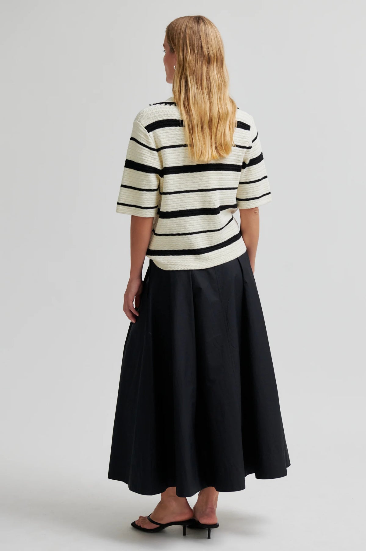 Woman wearing a black and white striped shirt and black skirt on a light gray background