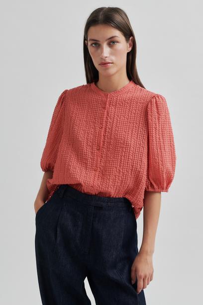 Woman wearing a coral checkered blouse and navy pants on a light gray background
