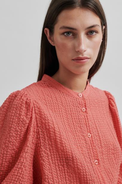 Woman wearing a coral checkered blouse on a light gray background