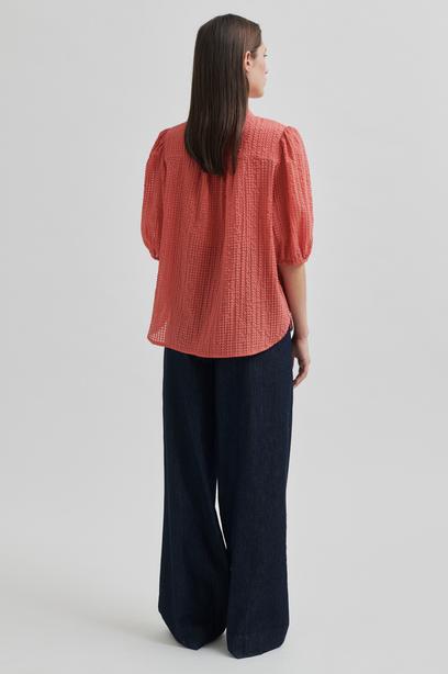 Woman wearing a coral checkered blouse and navy pants on a light gray background