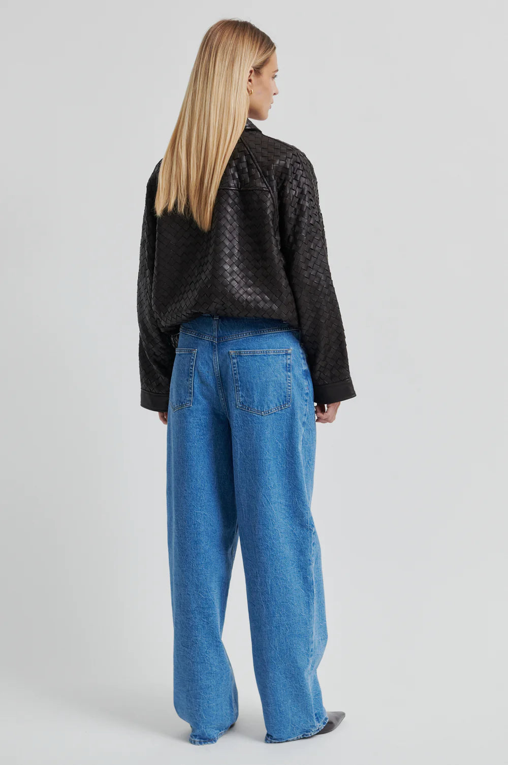 Model shown from the back wearing a Chocolate Brown woven leather jacket and denim jeans on a light background