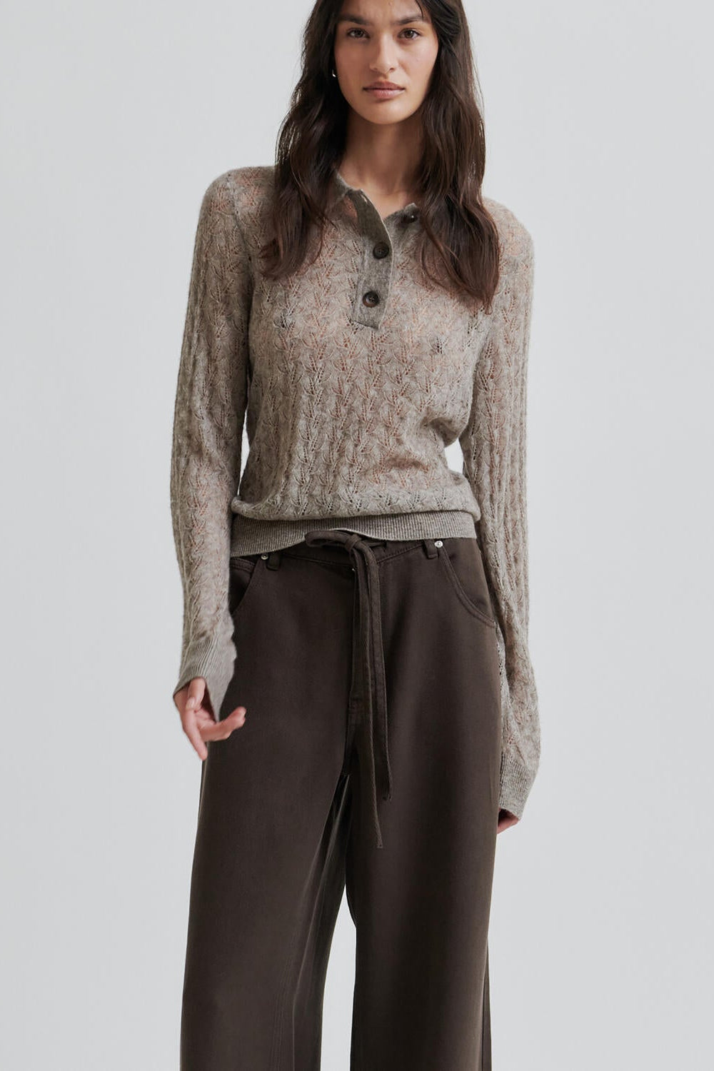 Woman wearing a patterned sweater and brown pants on a light gray background