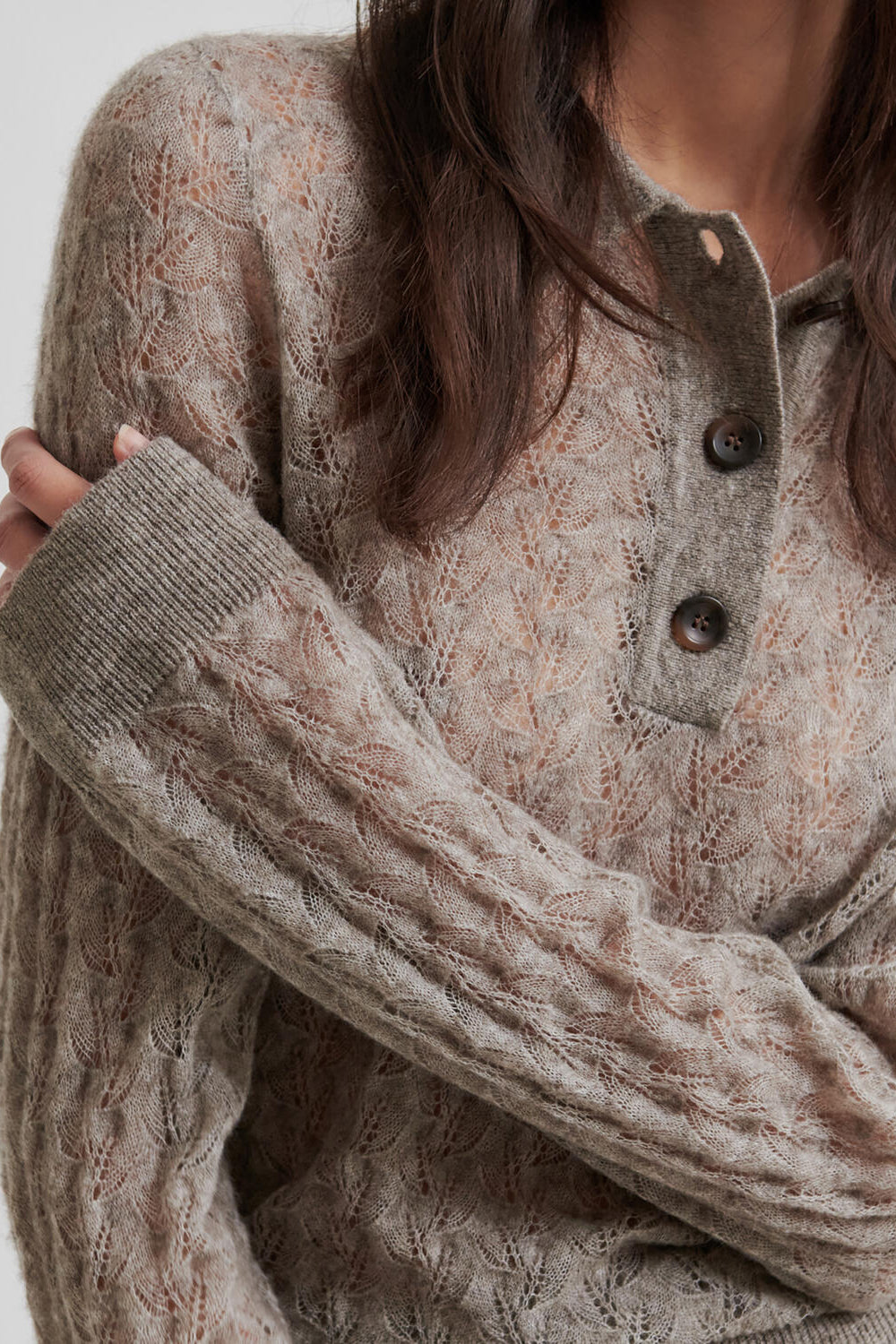 Person wearing a patterned sweater with button details on a plain background