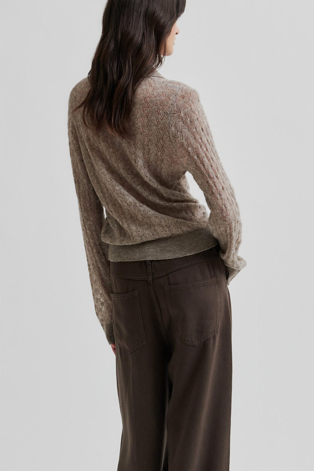 Person wearing a brown sweater and dark pants on a light gray background