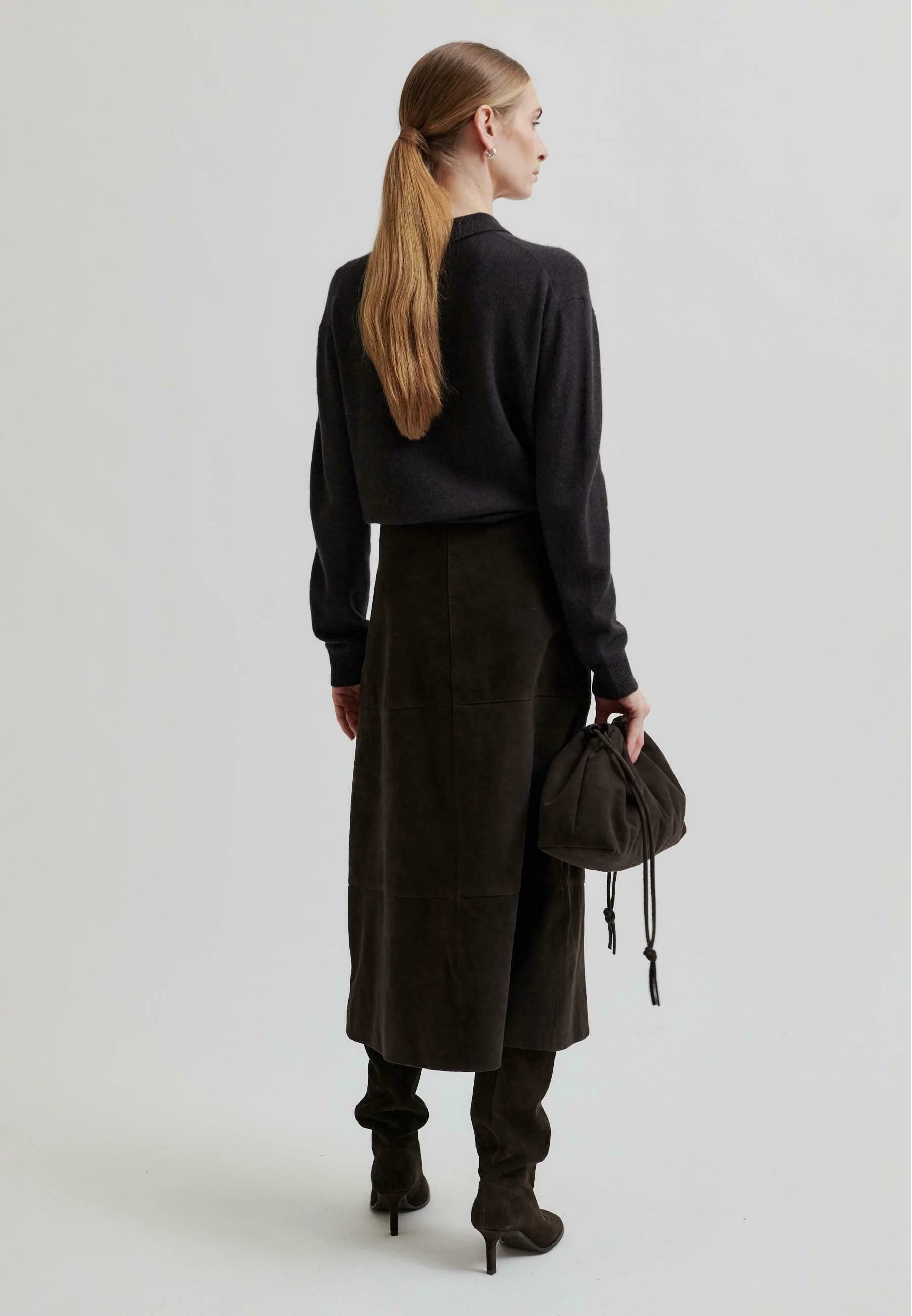 Woman wearing a chocolate brown ribbed sweater with with a long skirt on a white background