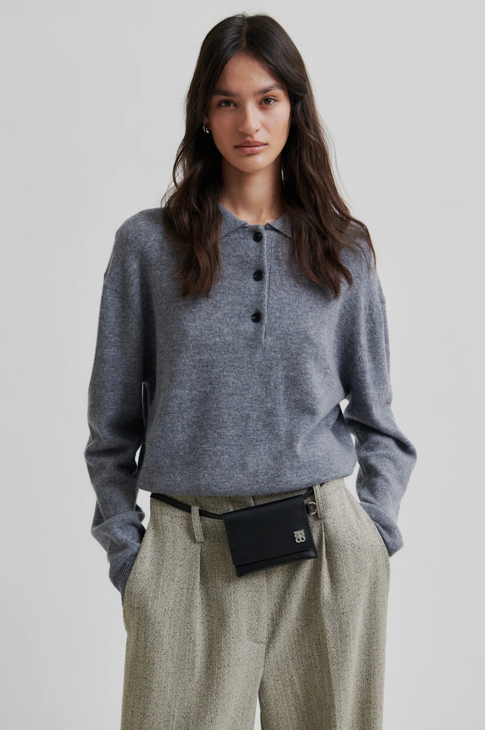 Woman wearing a grey polo neck sweater with black buttons and green pant on a white background. 