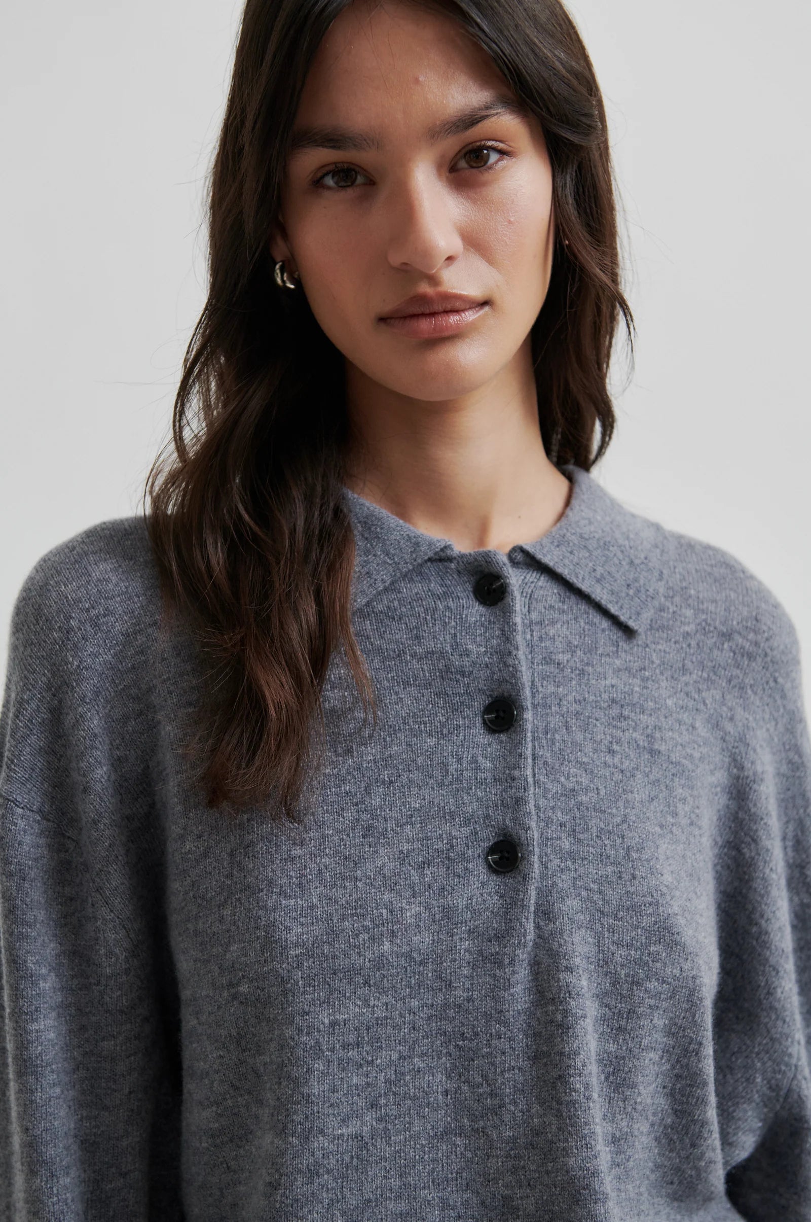 Woman wearing a grey polo neck sweater with black buttons and green pant on a white background. 