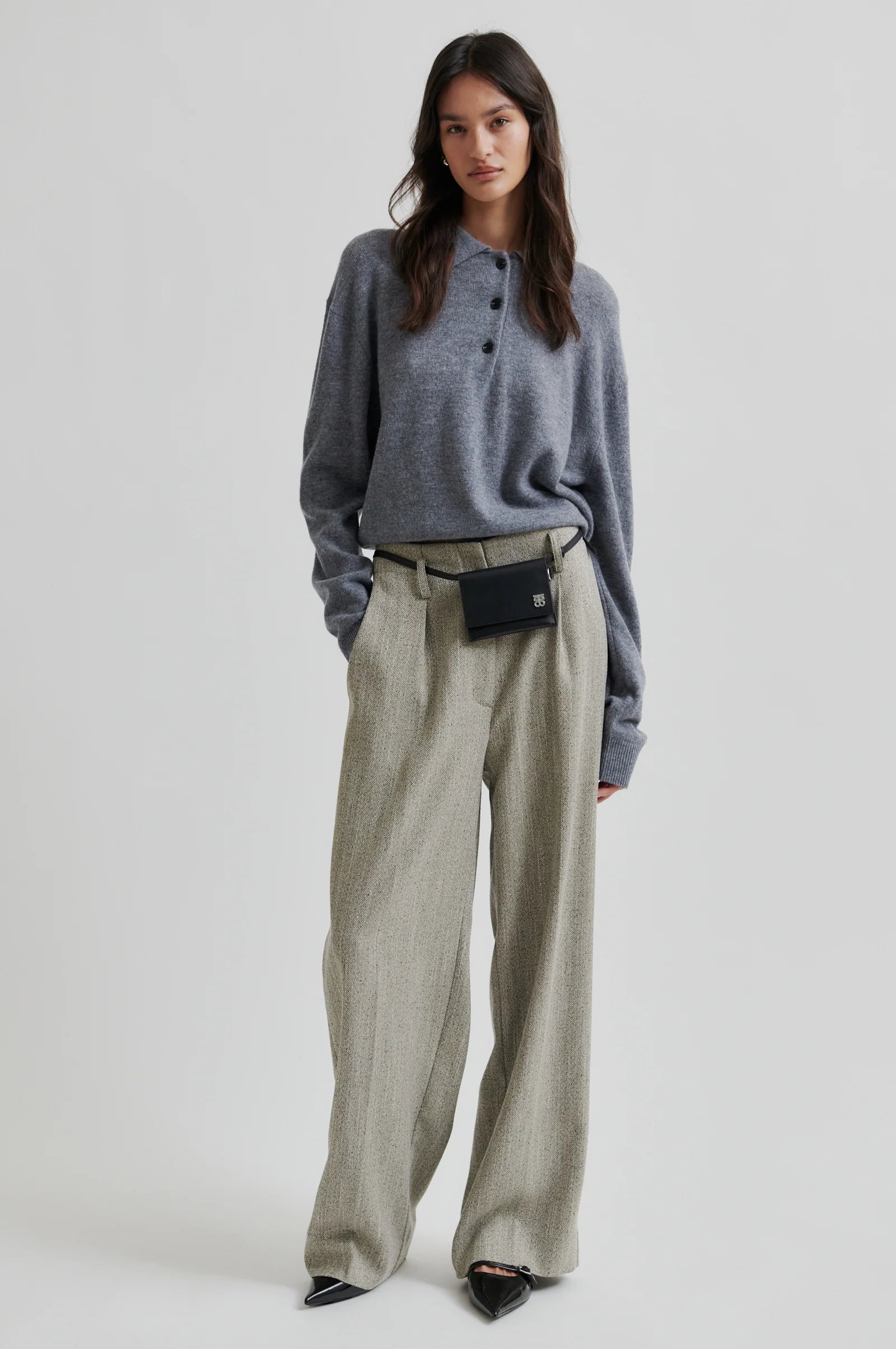 Woman wearing a grey polo neck sweater with black buttons and green pant on a white background. 