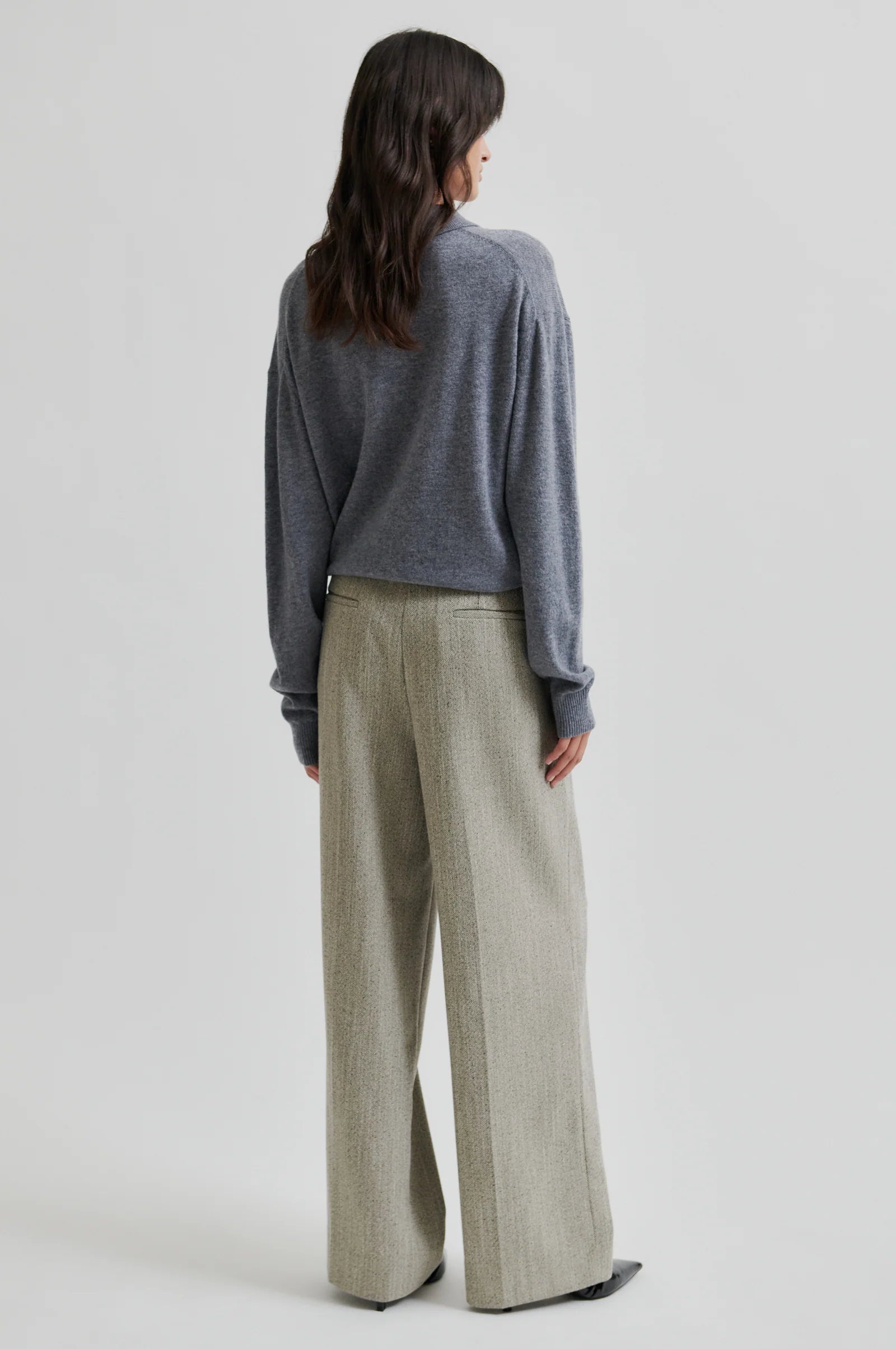 Woman wearing a grey polo neck sweater with black buttons and green pant on a white background. 