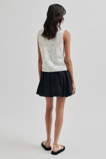 Woman wearing a white sleeveless top with black shorts on a white background
