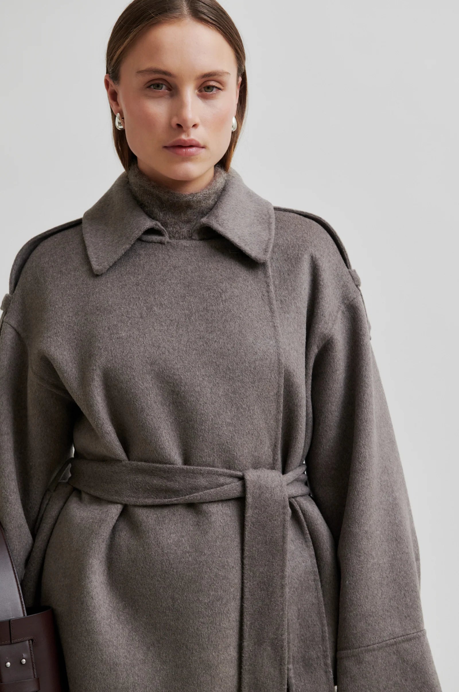Woman wearing a light brown coat with belt on a plain background