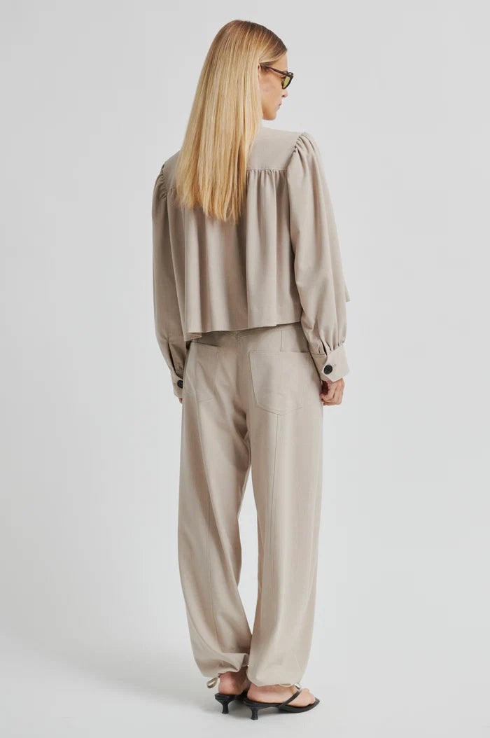 Lady shown from the back wearing beige wide-leg pants and top in same colour on a plain background