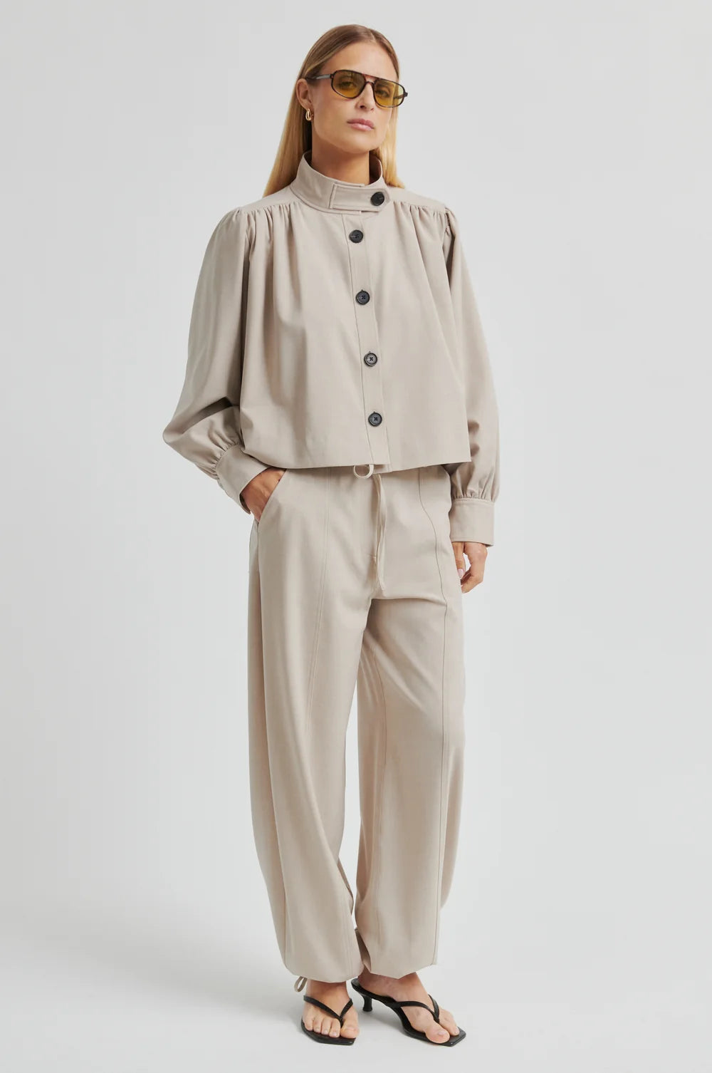 Lady wearing beige wide-leg pants and top in same colour on a plain background