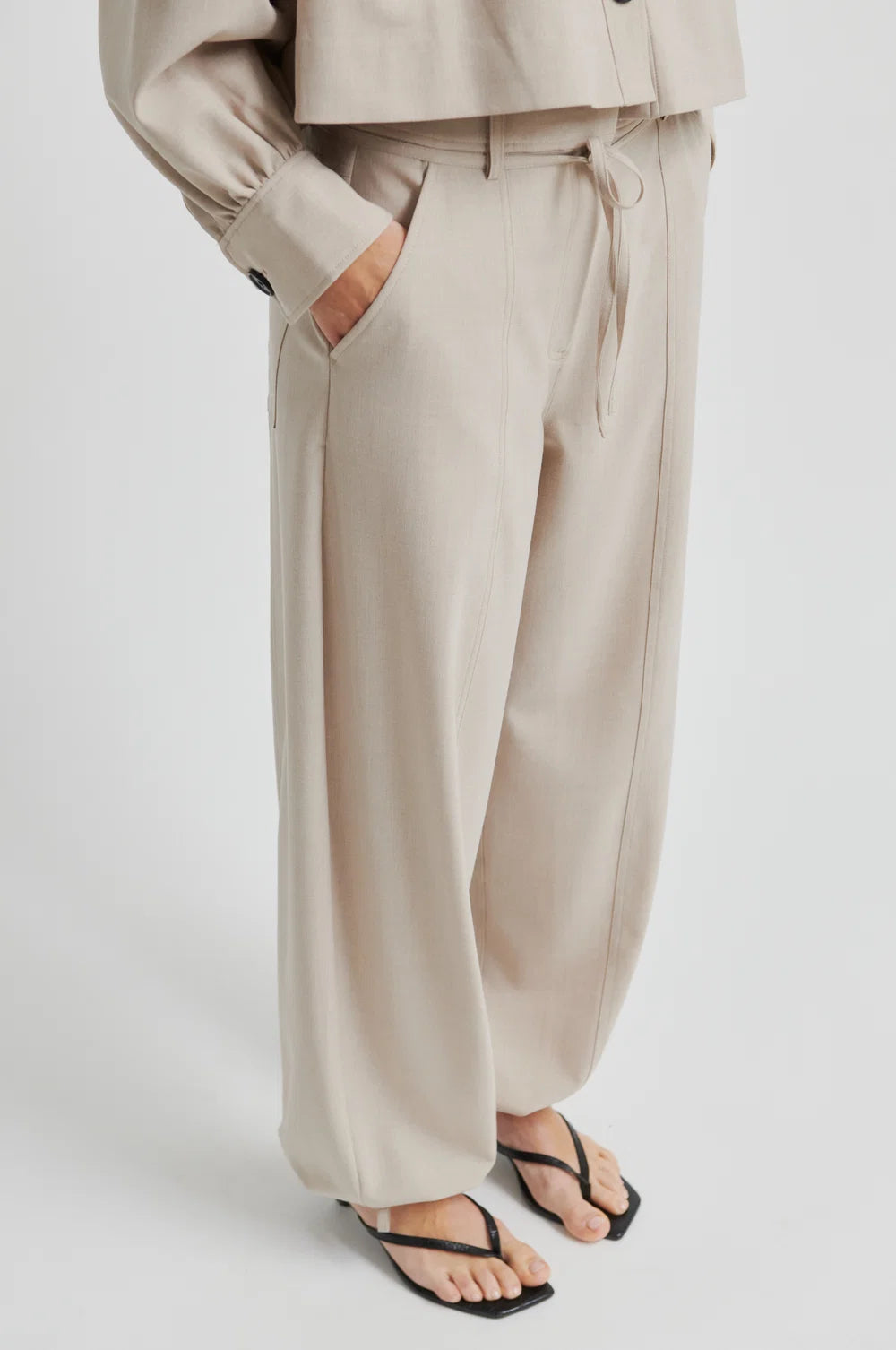 Lady wearing beige wide-leg pants and top in same colour on a plain background