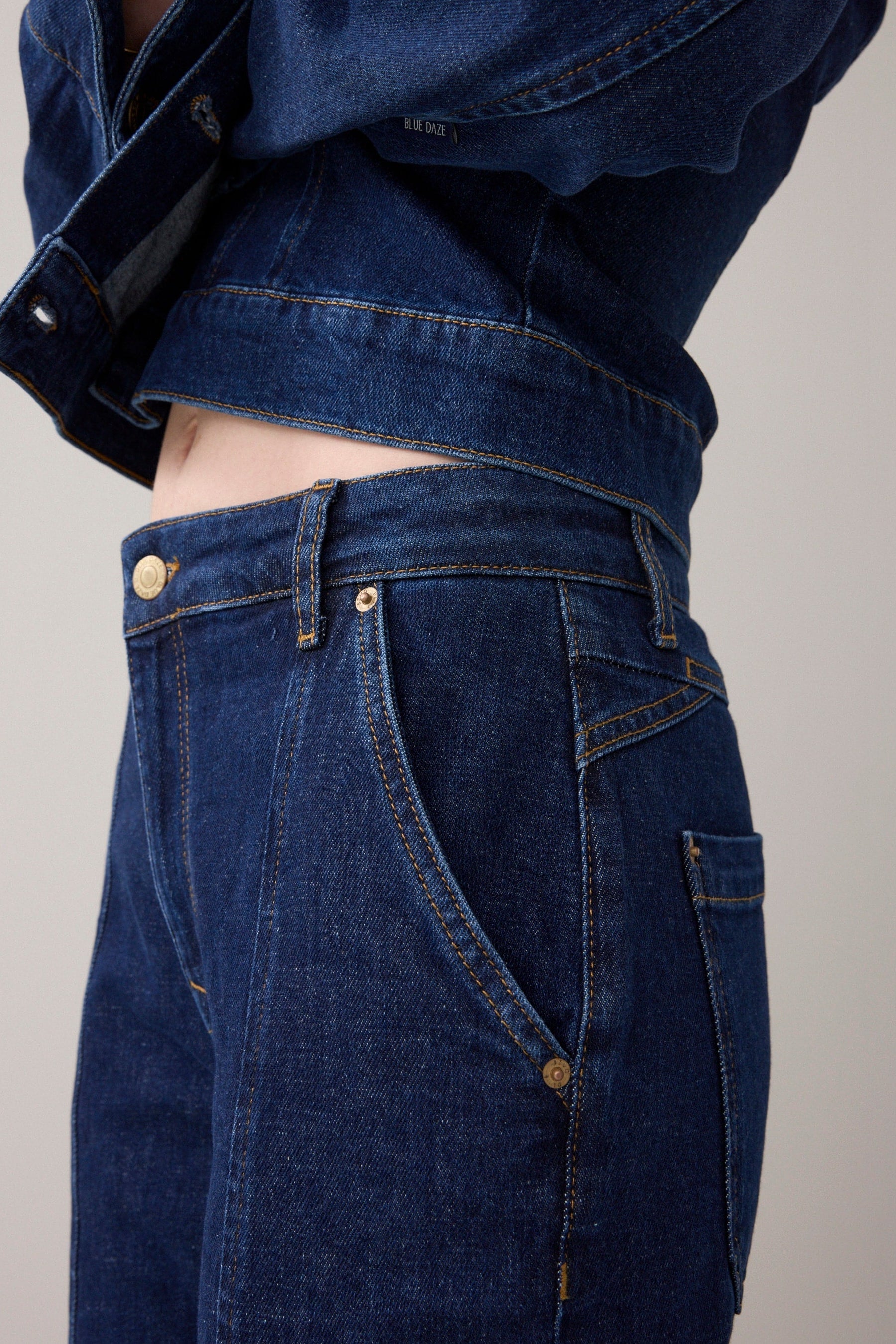 Close up of woman wearing a blue denim jacket and cropped jeans with slight flare  on a white background