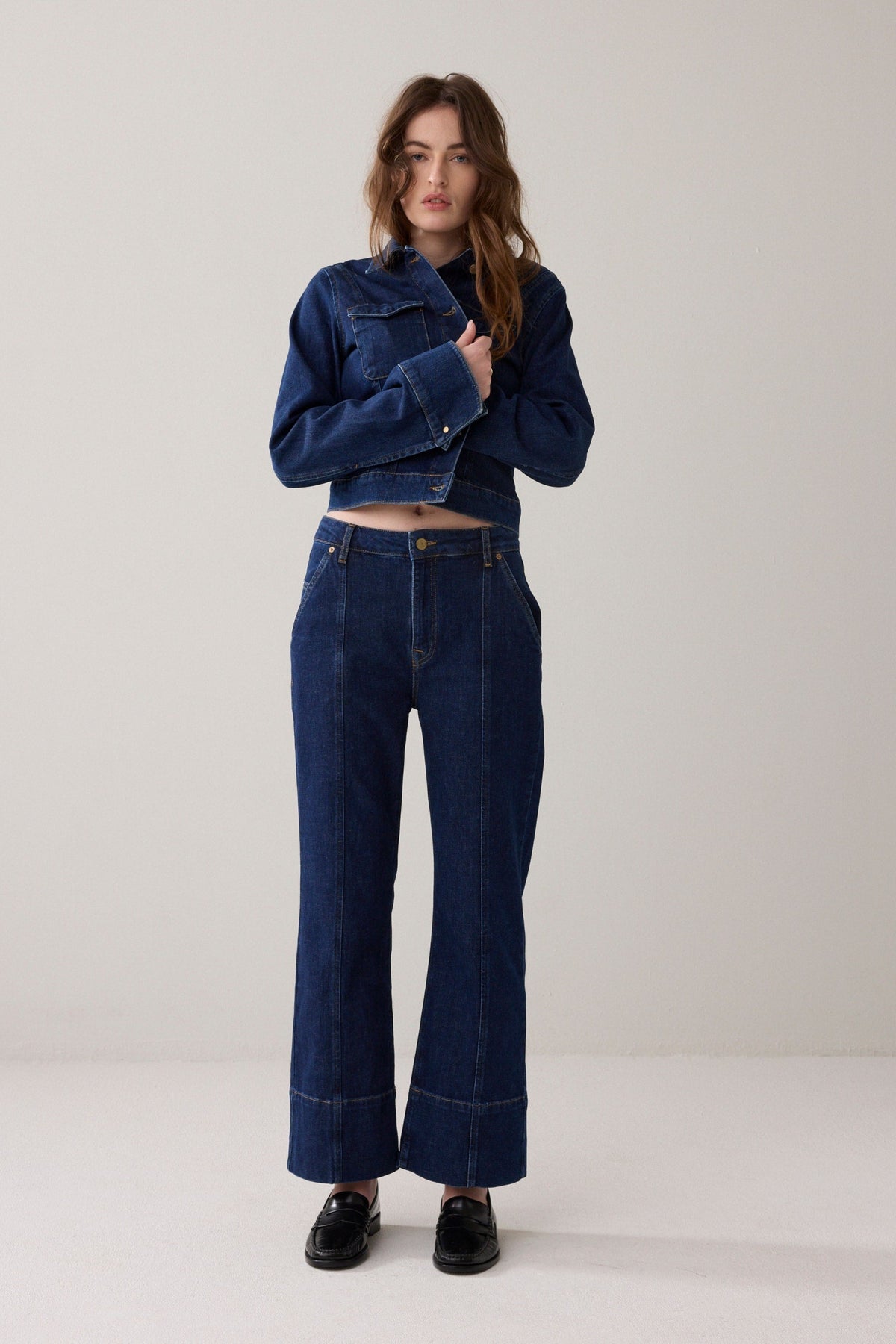 Woman wearing a blue denim jacket and cropped jeans with slight flare  on a white background