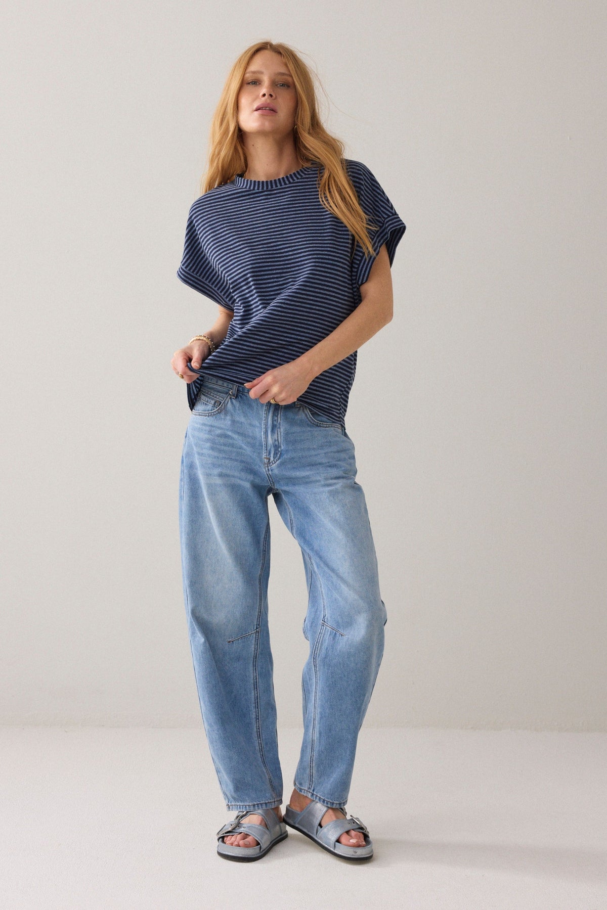 Women wearing a short-sleeve crewneck knit top with horizontal navy and light blue stripes and light blue jeans on a solid light beige background.