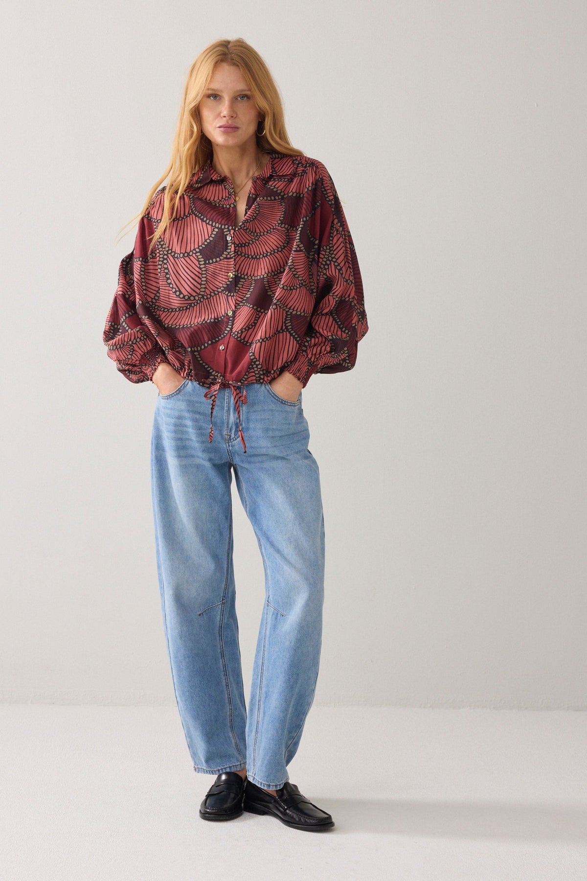 Woman wearing a patterned blouse and blue jeans on a plain background
