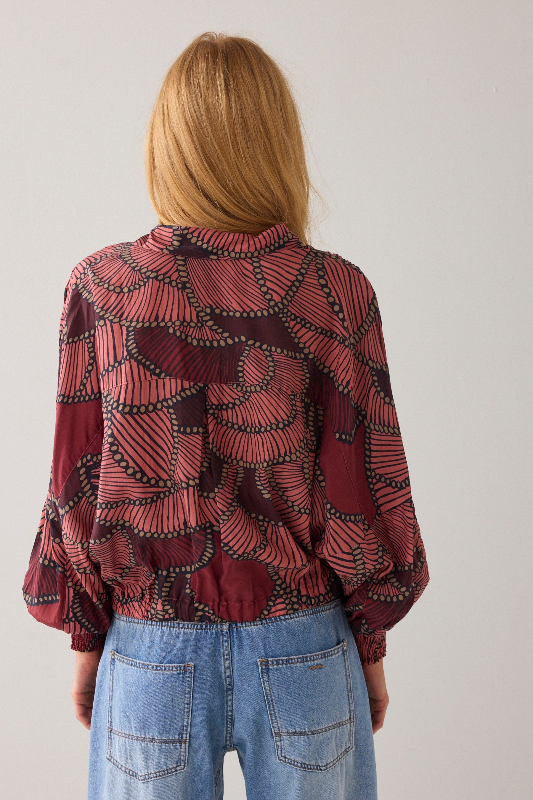 Women shown from the back wearing a patterned red blouse and blue jeans against a plain background