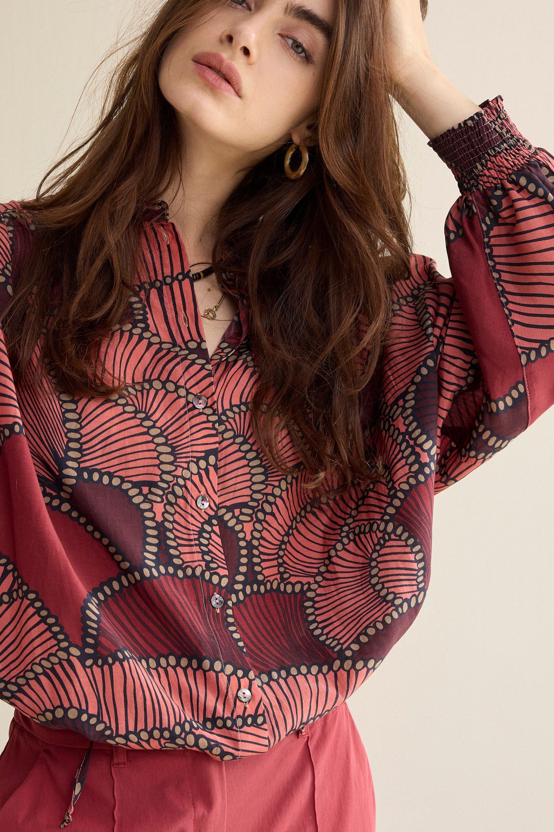 Woman wearing a red patterned blouse against a beige background