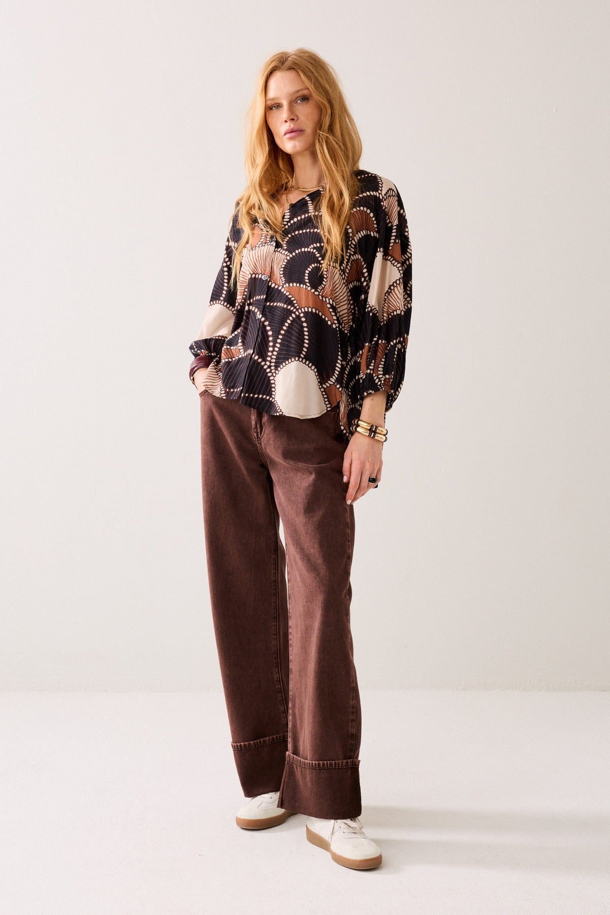 A women wearing a multi colour long-sleeve patterned shirt with brown pants on plain background