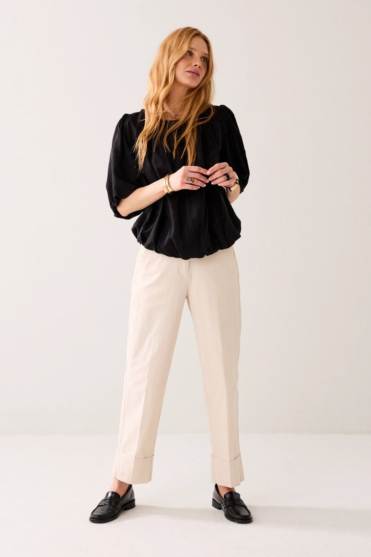 Model wearing a black blouse with puff sleeves  and cream tailored pants on a light background