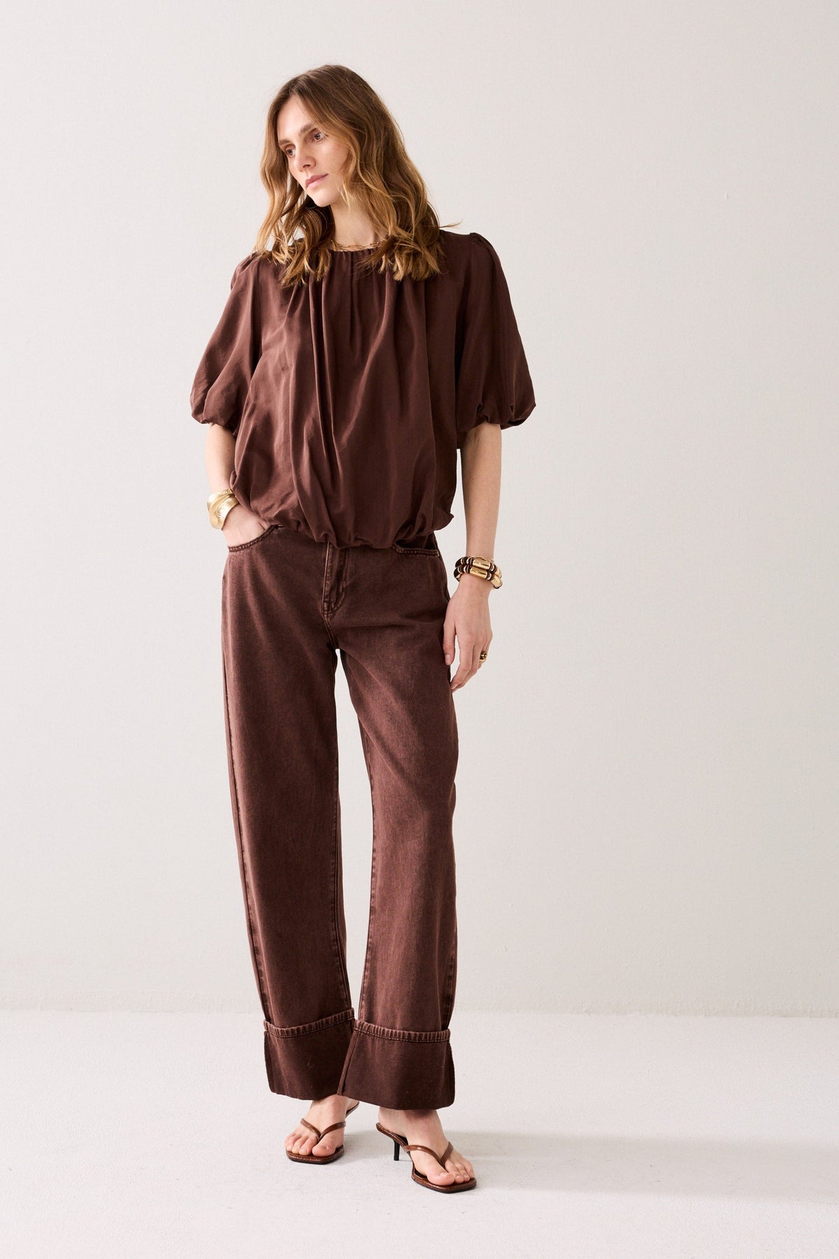 Women  wearing a brown blouse with short ballon sleeves on a light background