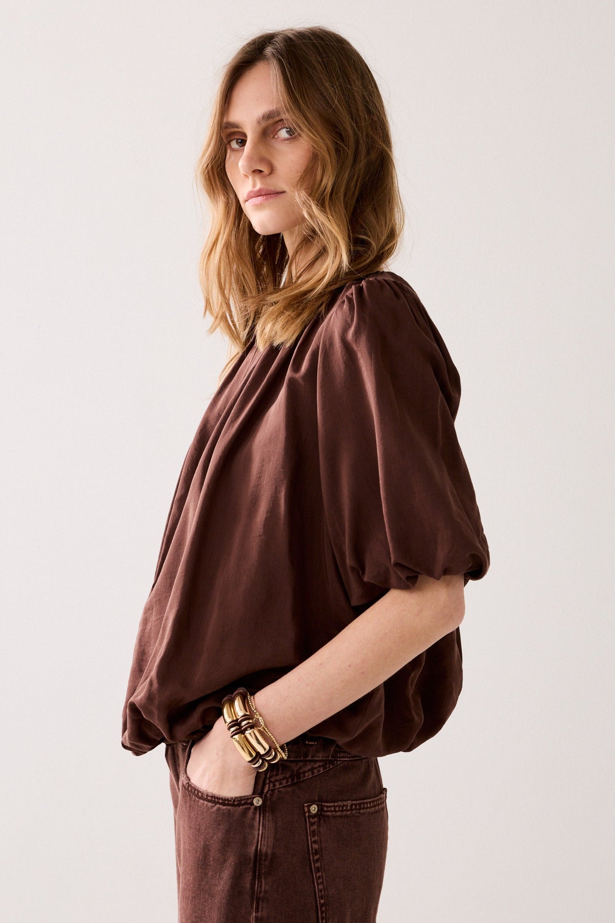 Women shown side on wearing a brown blouse with short ballon sleeves on a light background