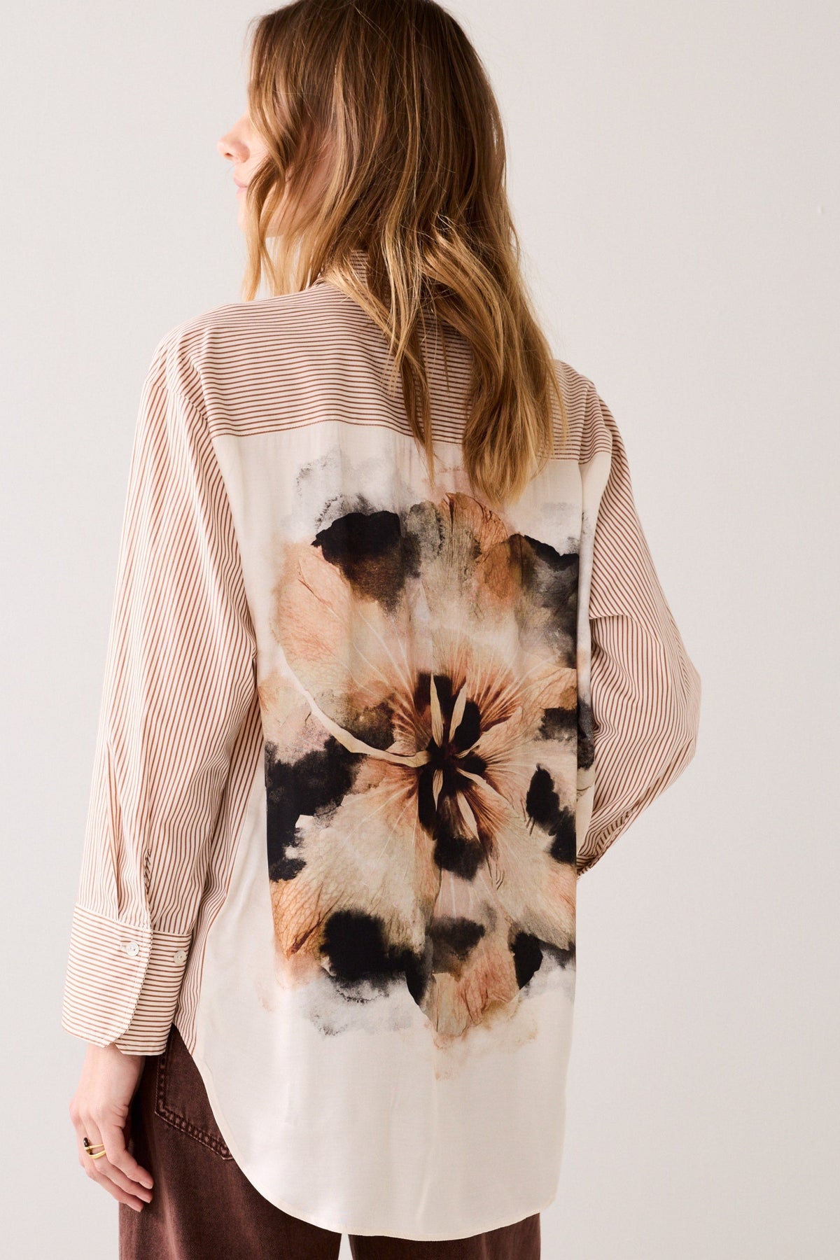 Woman wearing a floral patterned shirt  with a striped front and sleeves on a plain background