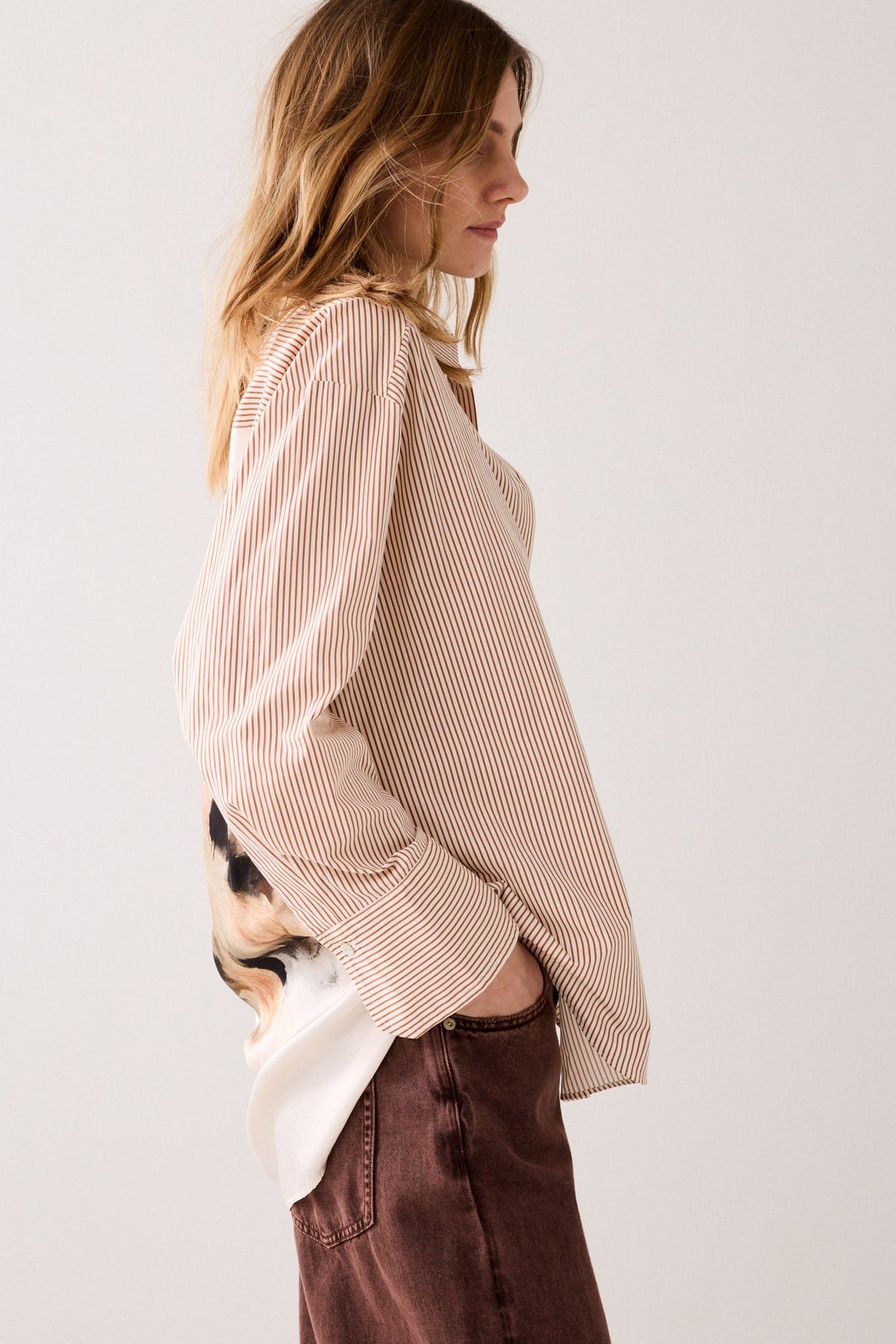 Woman wearing a beige striped shirt and brown pants against a plain background